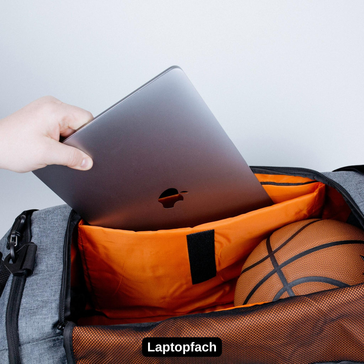 Gepolstertes Laptopfach der Ultimate Sportbag V4 – Laptop wird in das orange Innenfach der Sporttasche gesteckt